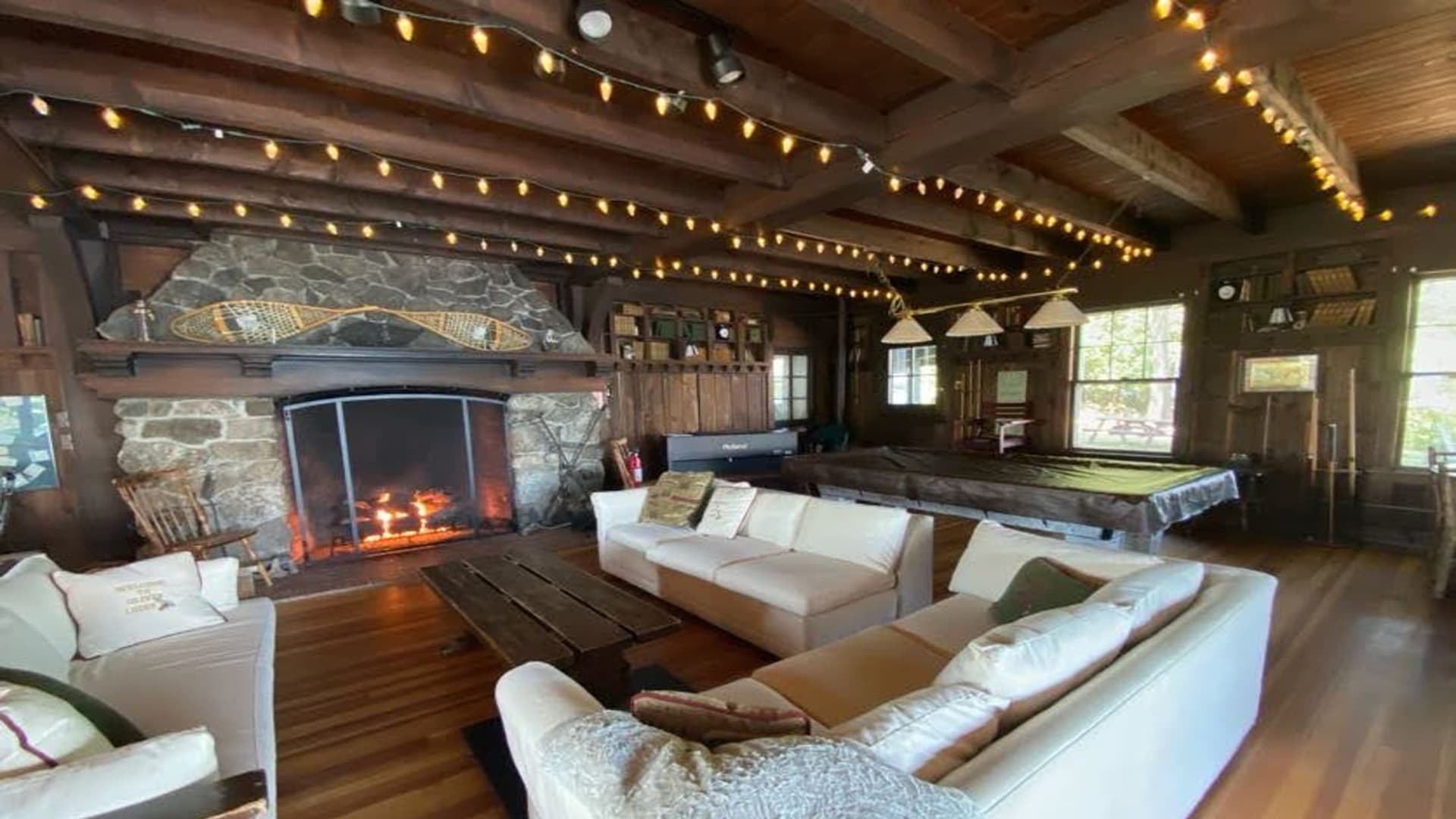 Cozy living room with a stone fireplace, wooden beams, and warm string lights.