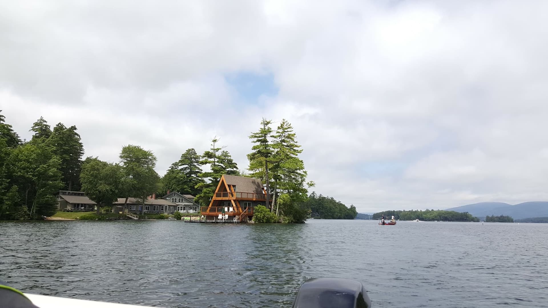 Lakeside view featuring a rustic cabin among trees, with a boat in the distance.