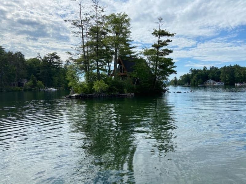 A secluded cabin surrounded by trees on a calm lake with a cloudy sky.